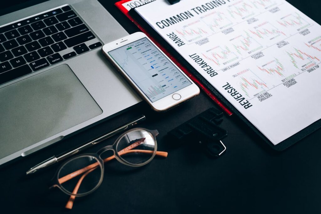 pexels photo 7887820 1 Workstation with laptop, smartphone, eyeglasses, financial charts, and pen for trading analysis.